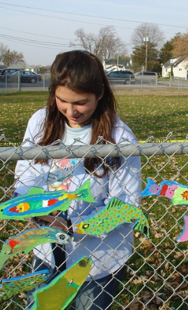 The dream fish are being installed on a chain link fence in front of a school.